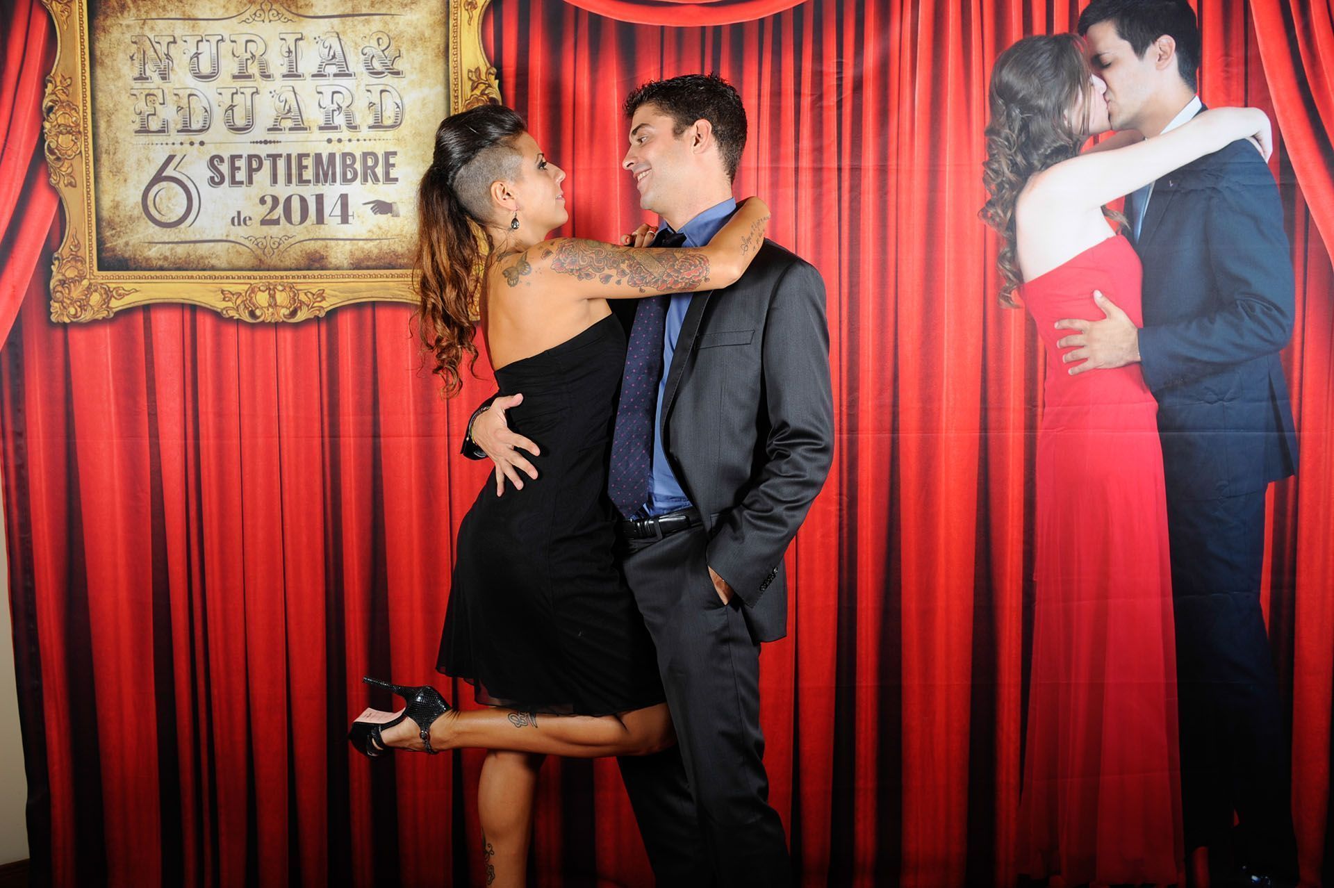 Pareja posando en un photocall personalizado con fondo de telón rojo para una boda.