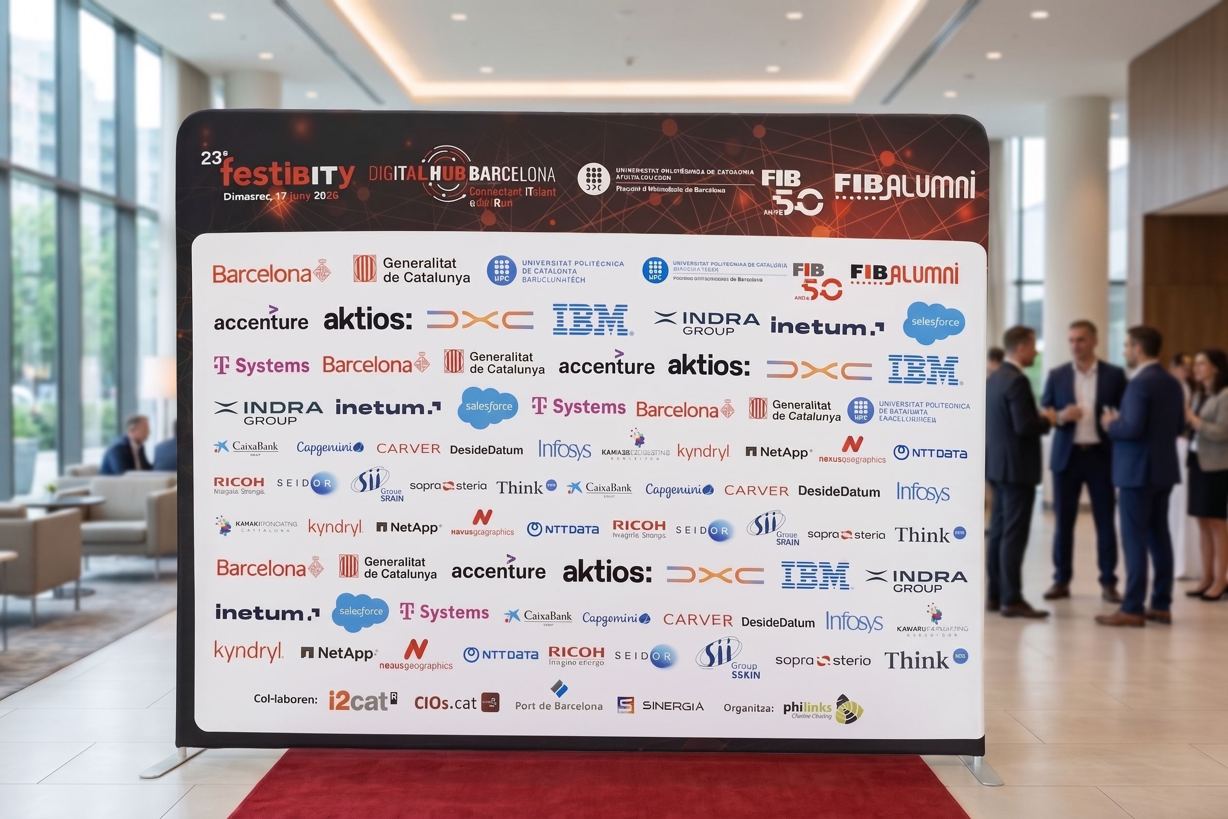 Un photocall para el evento '23º festiBITY Digital Hub Barcelona 2026', que muestra logotipos de la Generalitat de Catalunya, FIB Alumni, UPC y numerosas empresas colaboradoras como Accenture, IBM e Indra, situado sobre una alfombra roja en el hall de un edificio moderno con gente al fondo.